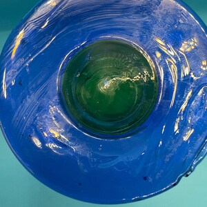 May include: A handcrafted glass bowl with a vibrant blue exterior and a green interior. The bowl's design features a circular shape with a smooth, glossy finish. The glass appears to have a textured, rippled effect, adding visual interest to the piece.