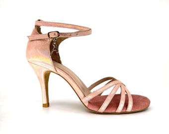 May include: Pink dance shoes with a delicate strap and a high heel. The shoes have a criss-cross design on the front and a suede sole.