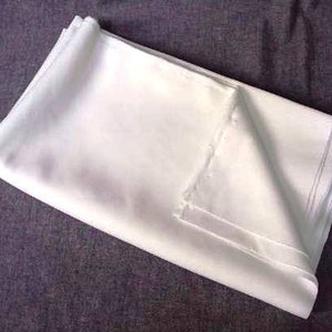 Peut inclure: Un tissu blanc plié, possiblement une nappe ou un drap, est posé sur une surface gris foncé. Le tissu semble lisse et propre, avec des plis et des coutures visibles. L'impression générale est celle d'un article net et fraîchement lavé.