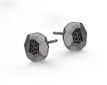 Puede incluir: Un par de pendientes de plata con un diseño geométrico y diamantes negros. Los pendientes están hechos de metal texturizado y tienen un aspecto moderno y único.