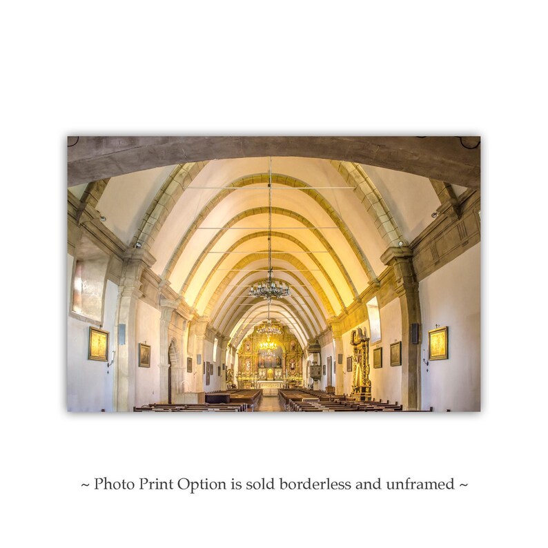 May include: A wide shot of the interior of a church with a vaulted ceiling and rows of pews. The ceiling is made of stone and has a series of arches. The pews are made of wood and are arranged in rows down the center of the church.