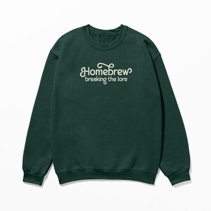 以下が含まれることがあります： 「Homebrew breaking the lore」と刺繍された白いロゴが付いた濃い緑色のスウェットシャツです。