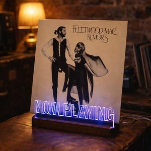 May include: A wooden record stand with a blue LED light that reads "NOW PLAYING" in front of a Fleetwood Mac "Rumours" album cover. The album cover features a black and white image of two people.