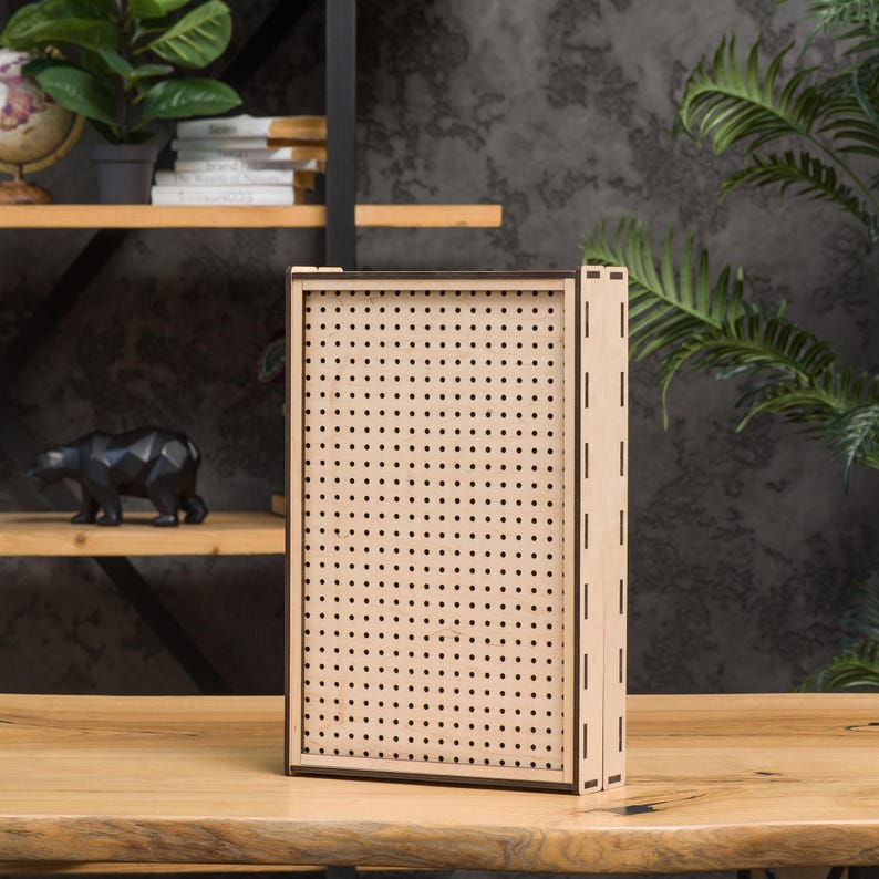 May include: A wooden box with a brown frame and a beige front panel with a grid of small holes. The box is sitting on a light brown wooden surface.