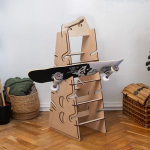 May include: A wooden skateboard rack with multiple shelves for storing skateboards. The rack is made of plywood and has a natural wood finish. The rack is designed to hold skateboards vertically, with the wheels facing out. The rack is shown with two skateboards, one of which is black with white text that reads "NEVER GIVE UP WITHOUT THE OTHER".