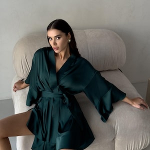 May include: A dark green satin robe with a tie belt and long sleeves. The robe has a relaxed fit and a V-neckline.