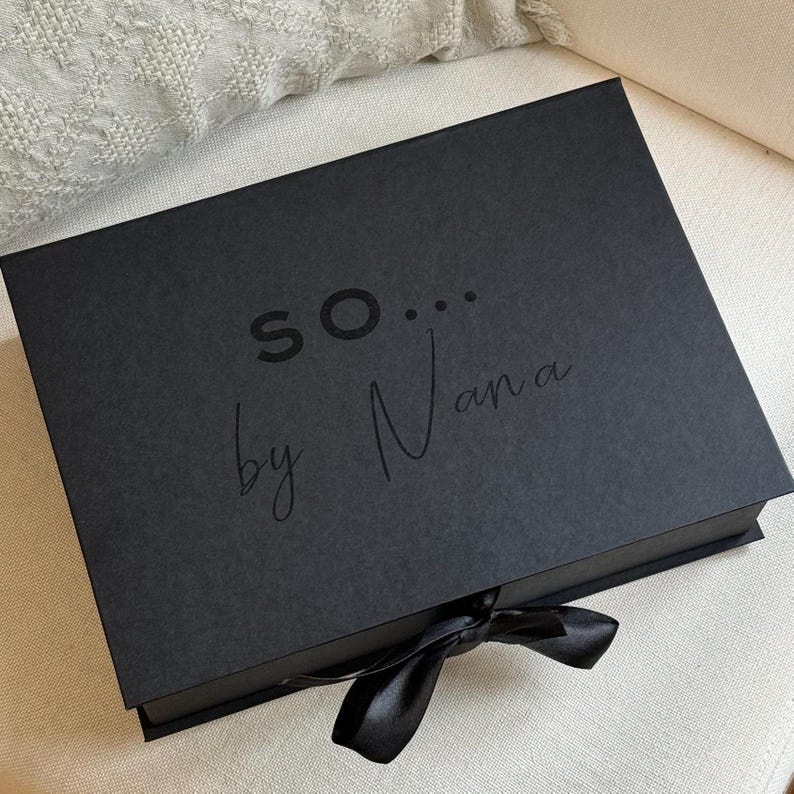May include: A black gift box with a black ribbon. The box has the text "SO... by Nana" printed on the top.