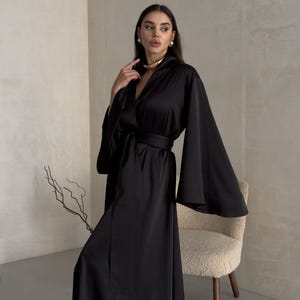 May include: A black satin robe with long sleeves and a wide sash. The robe has a deep V-neckline and a relaxed fit.