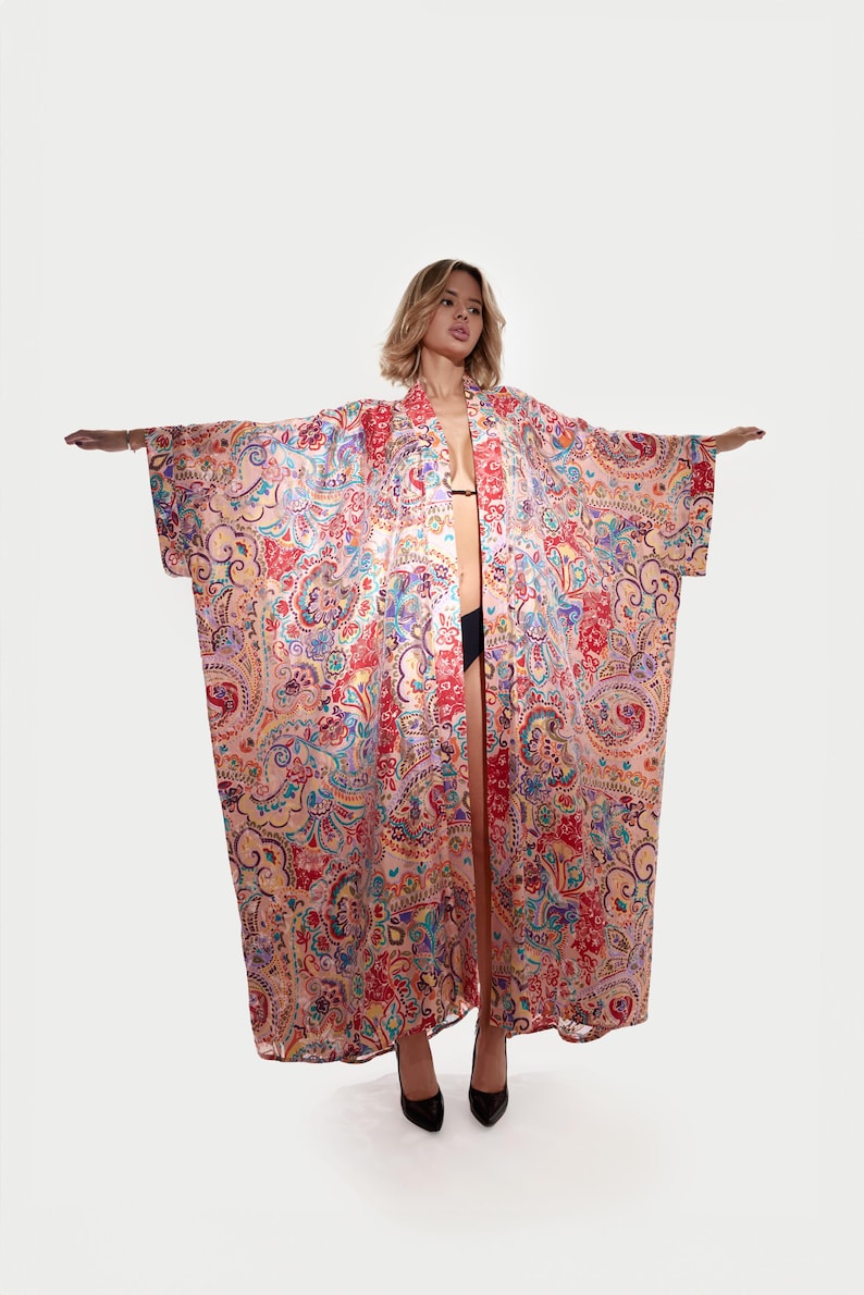 May include: A long, open-front kimono robe with a vibrant paisley pattern in shades of red, blue, and yellow. The robe is made of a lightweight fabric and has wide sleeves. The model is wearing black heels.