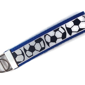 May include: A blue and white key chain with a repeating pattern of soccer balls. The key chain has a silver metal ring.
