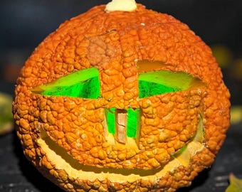 May include: A textured, orange, warty pumpkin carved into a jack-o'-lantern with a wide, smiling mouth and two triangular eyes. The carved openings are illuminated from within by a bright, vibrant green light, creating a glowing effect.