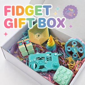 May include: A white gift box containing various plastic fidget toys, including a rainbow-colored hexagonal stacker, a rainbow cone, a light blue gear mechanism, a light blue square button pad, and a rainbow infinity cube, with text reading FIDGET GIFT BOX.