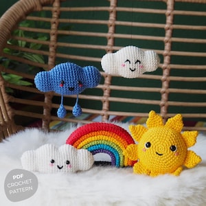 Può includere: Un set di giocattoli all'uncinetto a tema meteo, tra cui una nuvola blu con gocce di pioggia, due nuvole bianche, un arcobaleno e un sole giallo. I giocattoli hanno facce sorridenti.