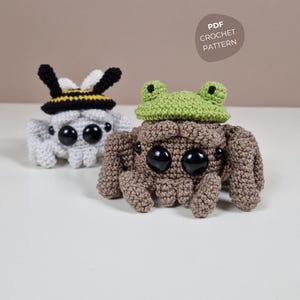 Könnte beinhalten: Zwei gehäkelte Spinnenspielzeuge. Eines ist grau mit einem Bienenhut, das andere ist braun mit einem grünen Froschhut. Beide haben große schwarze Augen. Der Text "PDF CROCHET PATTERN" befindet sich in einem Kreis oben rechts.