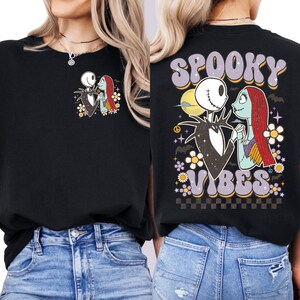 Puede incluir: Sudadera negra con un gr&aacute;fico de Jack Skellington y Sally de The Nightmare Before Christmas. La parte delantera tiene una imagen peque&ntilde;a, mientras que la parte trasera muestra "Spooky Vibes" en una fuente retro con detalles florales y a cuadros.