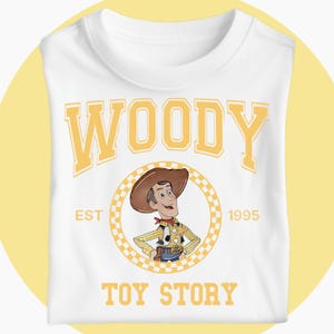 May include: White t-shirt with a cartoon illustration of Woody from Toy Story. The design features the word "WOODY" in yellow block letters above a circular image of the character, with "EST 1995" and "TOY STORY" below.