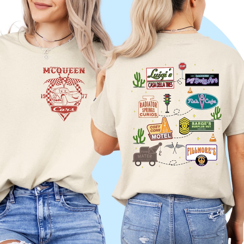 May include: A beige t-shirt with a Cars themed design. The front of the shirt features a red race car with the text "MCQUEEN 19 Cars 77". The back of the shirt features a map of Radiator Springs with various landmarks, including Luigi's Casa Della Tires, Flo's V8 Cafe, and Fillmore's.
