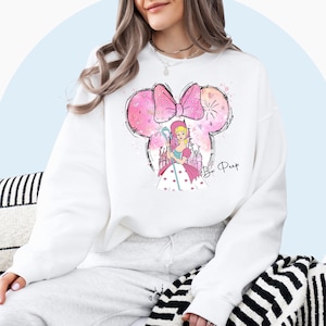 May include: White sweatshirt with a pink and white cartoon image of Bo Peep from Toy Story. The image includes a pink bow, a castle, and the text "Bo Peep".
