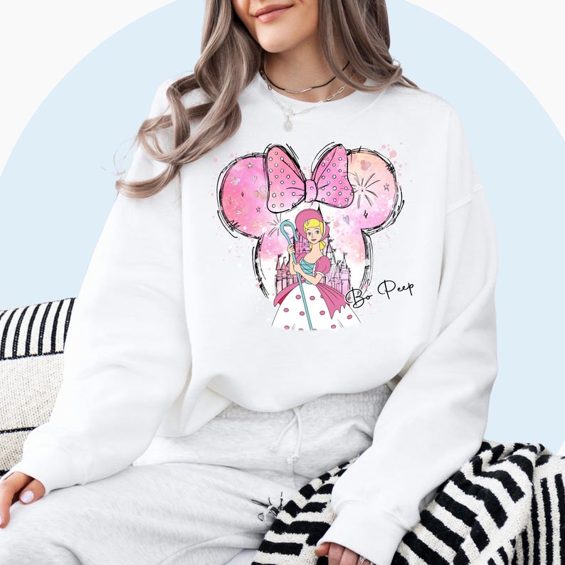 May include: White sweatshirt with a pink and white cartoon image of Bo Peep from Toy Story. The image includes a pink bow, a castle, and the text "Bo Peep".