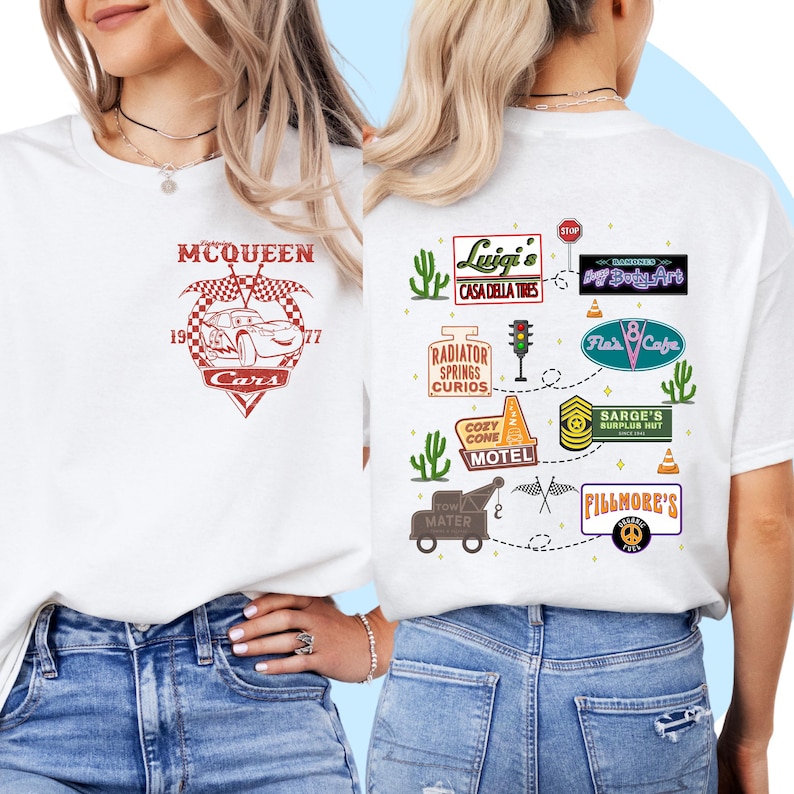 May include: White t-shirt with a red and white graphic of Lightning McQueen from the movie Cars. The back of the shirt features a map of Radiator Springs with various landmarks and businesses, including Luigi's Casa Della Tires, Cozy Cone Motel, and Fillmore's.