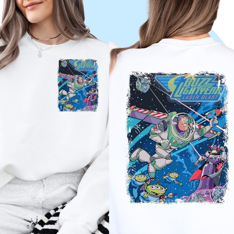 May include: White t-shirt with a colorful graphic print of Buzz Lightyear from the Toy Story franchise. The graphic features Buzz Lightyear in his spaceship, surrounded by other characters from the movie. The text "Buzz Lightyear Laser Blast" is printed on the graphic.