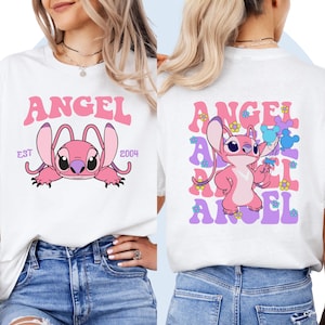 May include: White t-shirt with a pink cartoon character holding balloons. The character is surrounded by the word "ANGEL" in purple and pink letters. The text "EST 2004" is printed on the left side of the shirt.