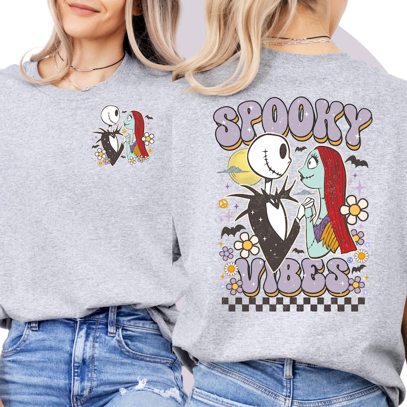 Puede incluir: Una sudadera gris claro con un dise&ntilde;o de Jack Skellington y Sally de The Nightmare Before Christmas. La parte delantera tiene una peque&ntilde;a imagen de los personajes, mientras que la parte trasera muestra "Spooky Vibes" en una fuente retro, con murci&eacute;lagos y flores.