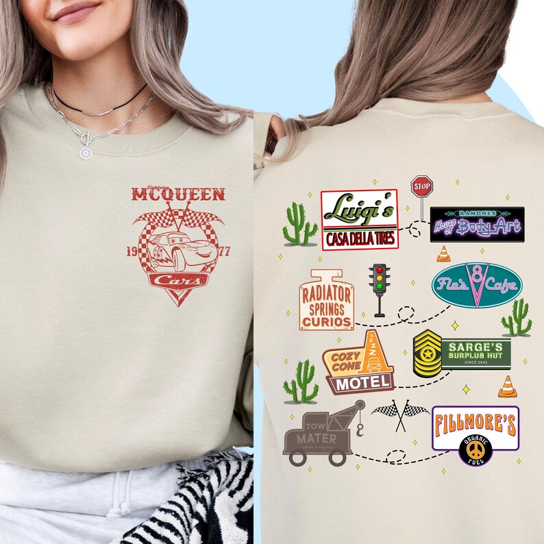 May include: A beige sweatshirt with a red and white graphic of Lightning McQueen from the Cars movie on the front. The back of the sweatshirt features a map of Radiator Springs with various landmarks and businesses from the movie, including Luigi's Casa Della Tires, Cozy Cone Motel, and Fillmore's.