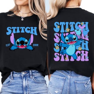 May include: Two black t-shirts with a blue Stitch character from Lilo & Stitch. One shirt has the text "Stitch" in a retro font with "EST 2002" below. The other shirt has the text "Stitch" repeated in a retro font with flowers and a blue Stitch character.