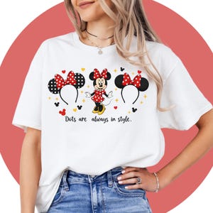 May include: White t-shirt featuring a Minnie Mouse design with polka dot bows and ears. The shirt includes the text "Dots are always in style." The design incorporates red, black, and yellow colors.