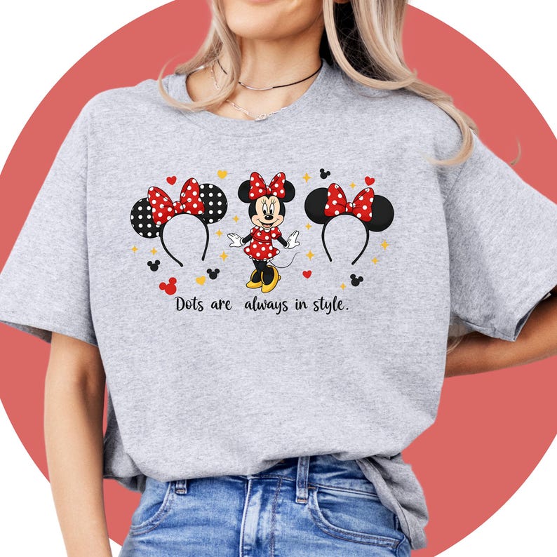 May include: A light gray t-shirt featuring a Minnie Mouse design. The design includes Minnie Mouse, her ears, and the text "Dots are always in style." The ears have red and black polka dot bows.