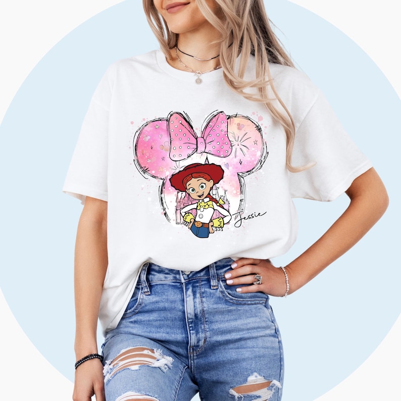 May include: White t-shirt with a pink and white Minnie Mouse ears design featuring a cartoon image of Jessie from Toy Story. The design includes a pink bow, fireworks, and the text "Jessie".