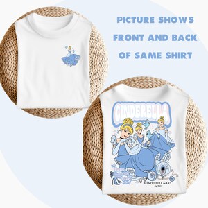 May include: White t-shirt featuring a graphic print of Cinderella in a blue dress and a crown. The text "Cinderella" is printed in pink and blue letters on the back of the shirt. The text "Let dream take you to where your heart belongs" is printed on the bottom of the shirt.