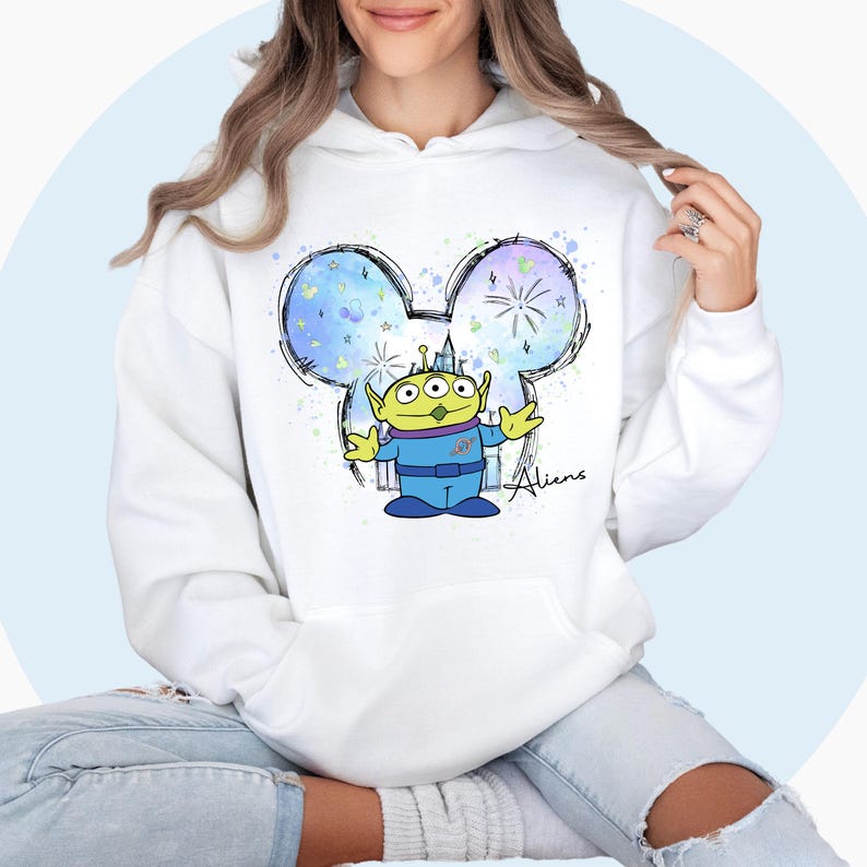 May include: White hoodie with a colorful graphic of a three-eyed alien with a blue spacesuit inside a Mickey Mouse head silhouette. The graphic also includes fireworks and a castle. The text "Aliens" is written below the graphic.