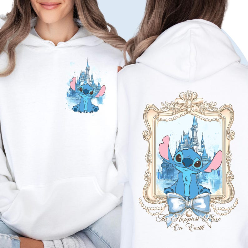 Puede incluir: Sudadera blanca con un personaje azul Stitch delante de una imagen de acuarela del castillo de Cenicienta. La parte posterior de la sudadera tiene un marco dorado con una imagen de acuarela del castillo de Cenicienta y Stitch delante. El texto "The Happiest Place On Earth" est&aacute; debajo del marco.