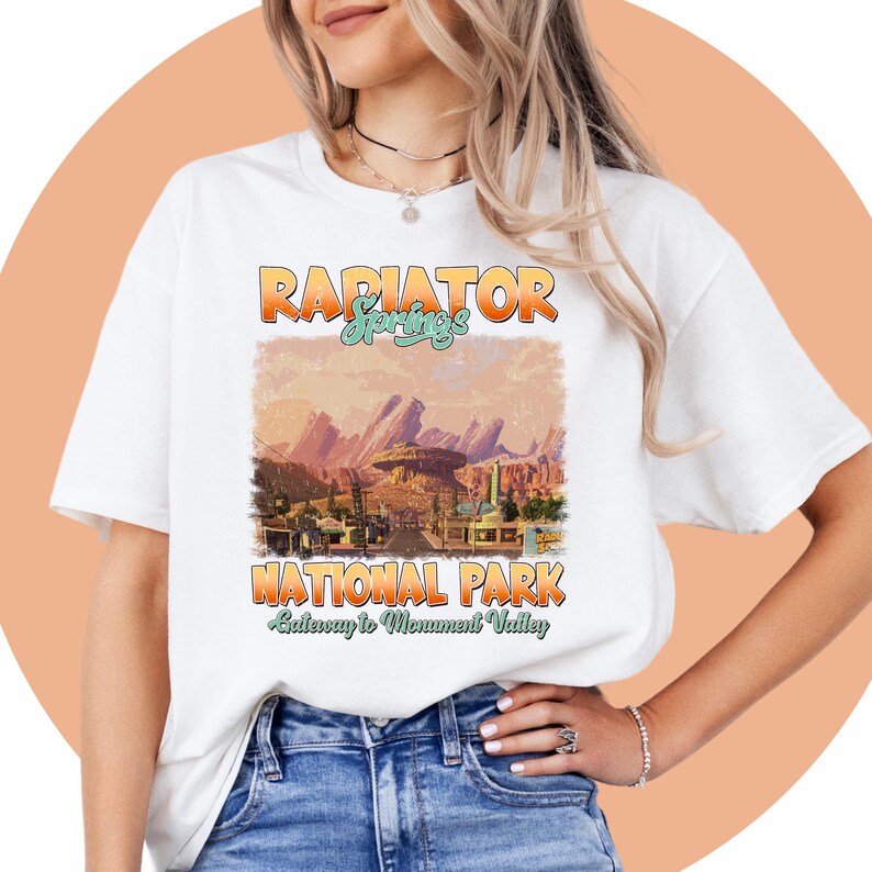May include: White t-shirt with a vintage-style graphic of Radiator Springs National Park, featuring the text "Radiator Springs National Park Gateway to Monument Valley".