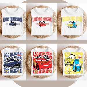 以下が含まれることがあります： 異なるカーズのキャラクターがプリントされた白いTシャツ6枚。シャツには、ドック・ハドソン、ライトニング・マックィーン、グイドとルイジが描かれています。一部のシャツには、チェッカーフラッグ柄の背景があります。
