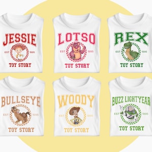 May include: White t-shirts featuring characters from the animated film Toy Story. Each shirt displays a character's name in a bold font, along with an image of the character, the text "EST 1995", and the words "TOY STORY".