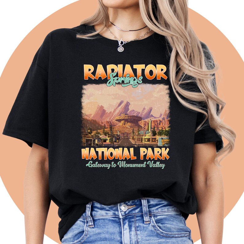 May include: Black t-shirt with a vintage-style graphic of Radiator Springs National Park, a gateway to Monument Valley. The graphic features a sunset scene with mountains and a road.