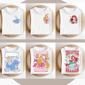 May include: Six white t-shirts featuring different Disney princess designs. The designs include Cinderella, Aurora, and Ariel. The shirts are all white with a variety of colours in the designs.