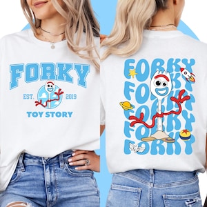 May include: White t-shirt with a blue and red cartoon character on the front. The character is a fork with a face and arms. The text "Forky Est. 2019 Toy Story" is printed on the shirt. The back of the shirt has the word "Forky" printed in blue multiple times.