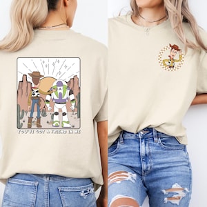 Puede incluir: Dos mujeres con camisetas beis con una imagen de dibujos animados de Woody y Buzz Lightyear de Toy Story. El texto de la camiseta dice "You've got a friend in me". Una camiseta tiene una pequeña imagen de Woody en la parte delantera. Ambas mujeres llevan pantalones vaqueros azules.