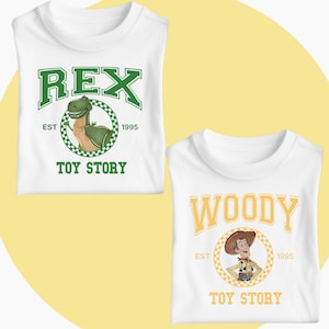 May include: Two white t-shirts with Toy Story designs. One displays "REX" in green lettering with a cartoon dinosaur. The other has "WOODY" in gold letters with a cartoon cowboy. Both shirts feature "TOY STORY" and "EST 1995".
