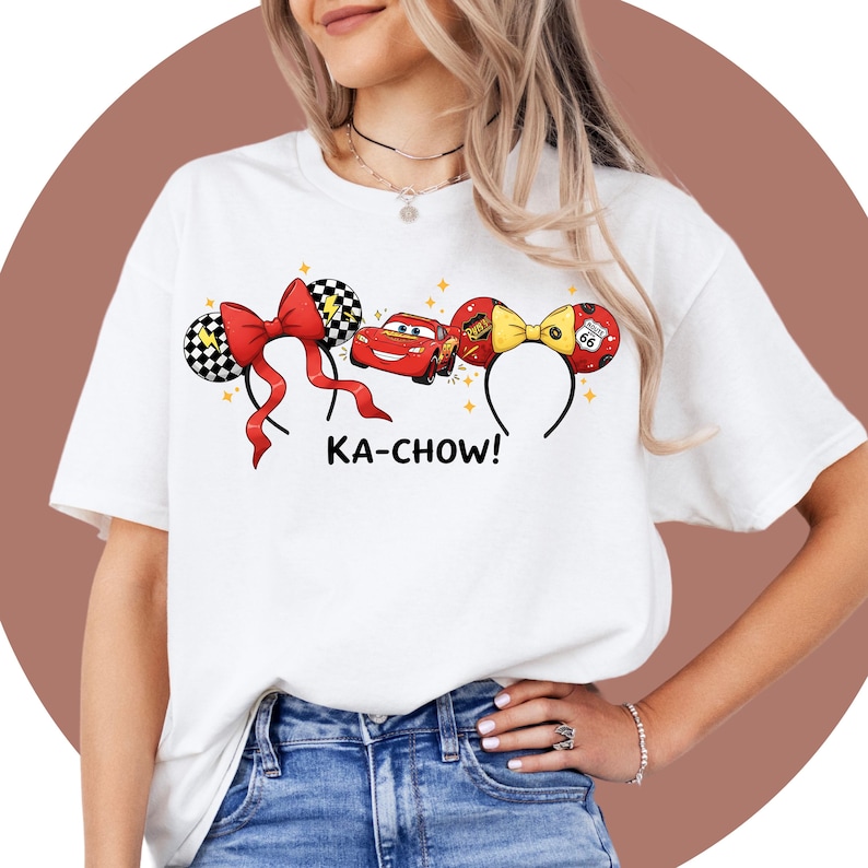 May include: White t-shirt featuring a design with a red bow, a red car, and a yellow bow with the text "KA-CHOW!". The design includes black and white checkered ears and a Route 66 sign. The shirt is a casual wear item.