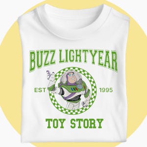 May include: White t-shirt with a green graphic of Buzz Lightyear from Toy Story. The design includes the text "BUZZ LIGHTYEAR", a circular image of the character, and the text "EST 1995" and "TOY STORY".