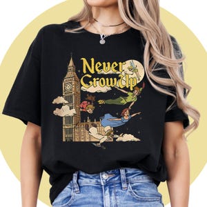 May include: Black t-shirt with a colourful illustration of Peter Pan, Wendy, John, Michael, and Tinkerbell flying near Big Ben. The text "Never Grow Up" is in a yellow, vintage font.