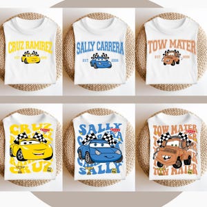 以下が含まれることがあります： ディズニーピクサー映画「カーズ」のキャラクターをフィーチャーした、異なるデザインの白いTシャツ6枚。デザインには、クルーズ・ラミレス、サリー・カレラ、メーターが含まれています。一部のデザインには、キャラクターが市松模様の旗を持ち、「クルーズ」、「サリー」、「メーター」というテキストがパターンで繰り返されています。