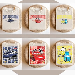 Puede incluir: Seis camisetas diferentes con personajes de la franquicia de pel&iacute;culas Cars de Disney Pixar. Las camisetas presentan a Doc Hudson, Rayo McQueen y Mate. Las camisetas son todas blancas con gr&aacute;ficos coloridos. El texto en las camisetas dice "Doc Hudson", "Rayo McQueen" y "Mate".