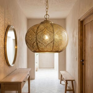 Könnte beinhalten: Ein Flur mit einer großen, verzierten goldenen Pendelleuchte. Das Licht wirft komplizierte Muster an die Wände. Eine Holzkonsolentisch und eine Bank sind ebenfalls zu sehen.