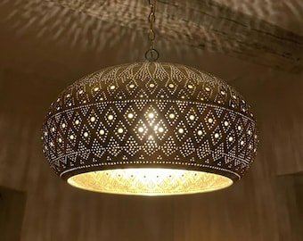 May include: A decorative, hanging pendant light with a perforated metal shade. The shade is a warm gold color and features a pattern of diamond and dot cutouts. The light hangs from a chain and illuminates the surrounding area.